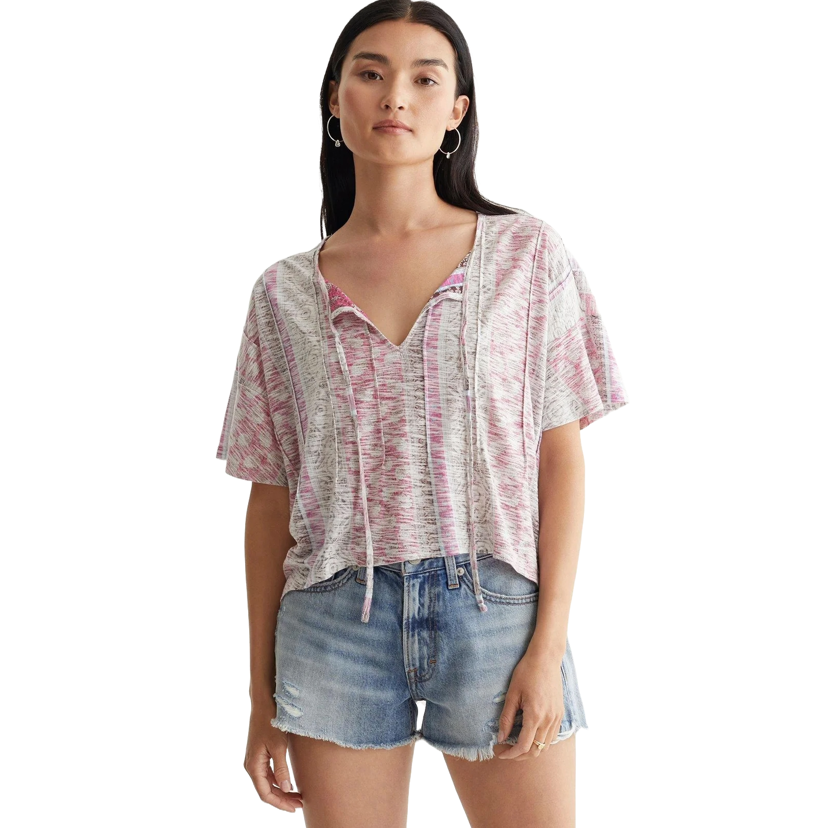 A woman wearing a loose, short-sleeve, pink and white patterned top with drawstrings and distressed denim shorts.