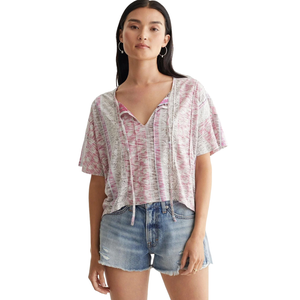 A woman wearing a loose, short-sleeve, pink and white patterned top with drawstrings and distressed denim shorts.