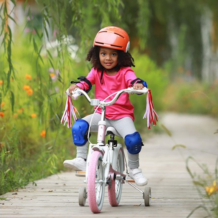 Child riding a bicycle with training wheels, wearing a helmet and knee pads.