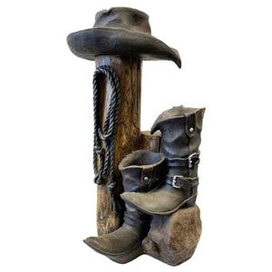 A decorative fountain featuring a cowboy hat, boots, and a coiled rope around a wooden post, designed with an LED light to create a rustic, western-themed outdoor ambiance.