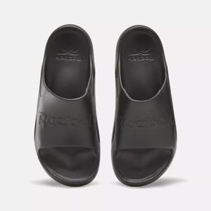 A pair of black Reebok slide sandals with the brand name embossed on the top.