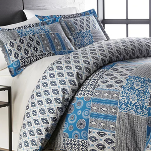 A queen-sized comforter set with a patchwork design featuring a mix of blue and gray patterns on the pillows and comforter.