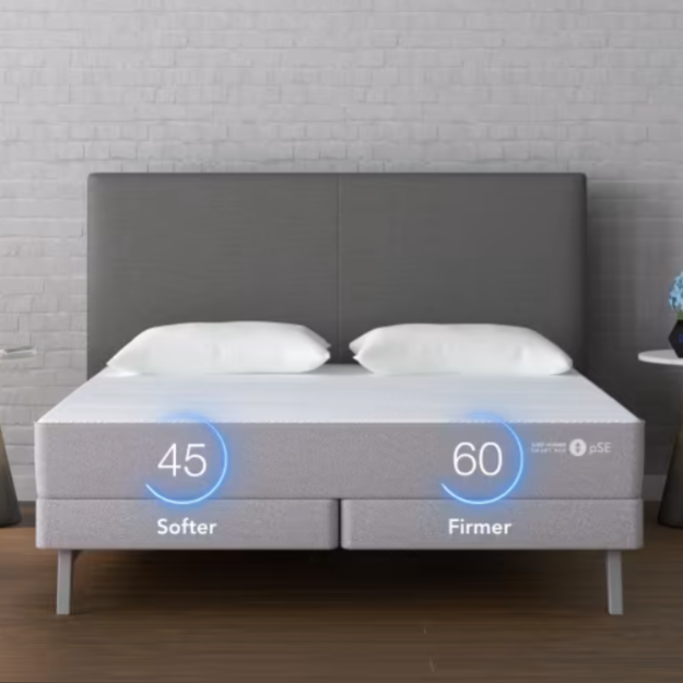 A split mattress is shown with adjustable firmness levels, displaying a softer side at 45 and a firmer side at 60, alongside two bedside tables with lighting and decor.