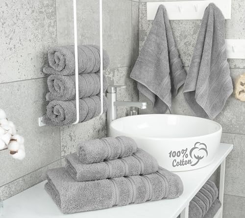 Gray Turkish cotton towels are arranged neatly, with some rolled and others hanging, showcasing their plush texture. A white basin displays the \“100% Cotton\“ label, emphasizing the material's quality.