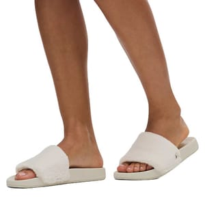 Fluffy white open-toe slide sandals with a thick sole are being worn by a person with tan skin.