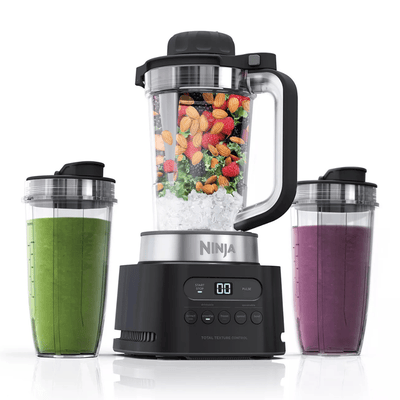 A Ninja blender with a main blending container filled with fruits, vegetables, nuts, and ice, accompanied by two to-go cups with green and purple smoothies.