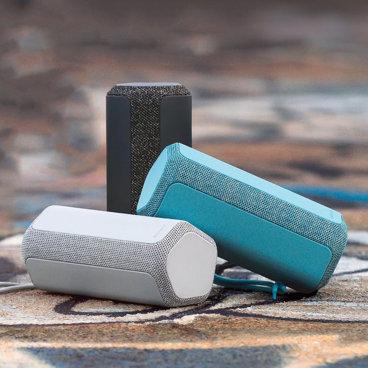 Three portable wireless speakers in varying colors and orientations.