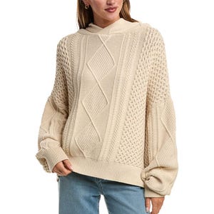A beige cable-knit sweater with a hood and oversized sleeves is paired with blue jeans.