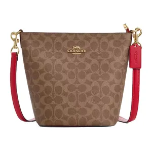 A Coach handbag with a signature brown monogram pattern and a red leather strap. The bag features gold-tone hardware and a Coach logo tag.