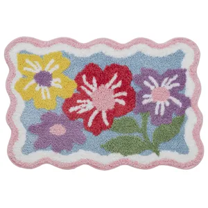 A colorful rectangular rug with a scalloped pink border, featuring a floral design with red, yellow, and purple flowers on a blue background.