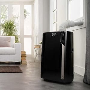 A black portable air conditioner with a digital display is situated in a room beside a window, connected to a vent hose.