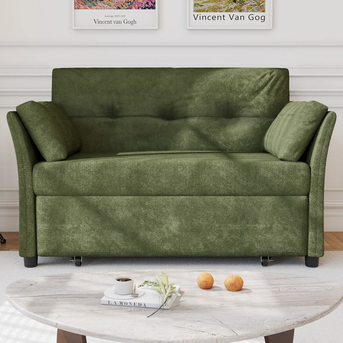 A green loveseat with two side cushions is placed in a living room with a marble coffee table in front, holding a cup, book, and two fruits. Van Gogh posters are on the wall behind.
