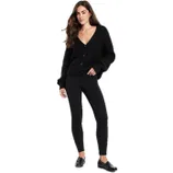 A woman is wearing a black knit cardigan with a V-neck and buttoned front, paired with black leggings and black loafers.