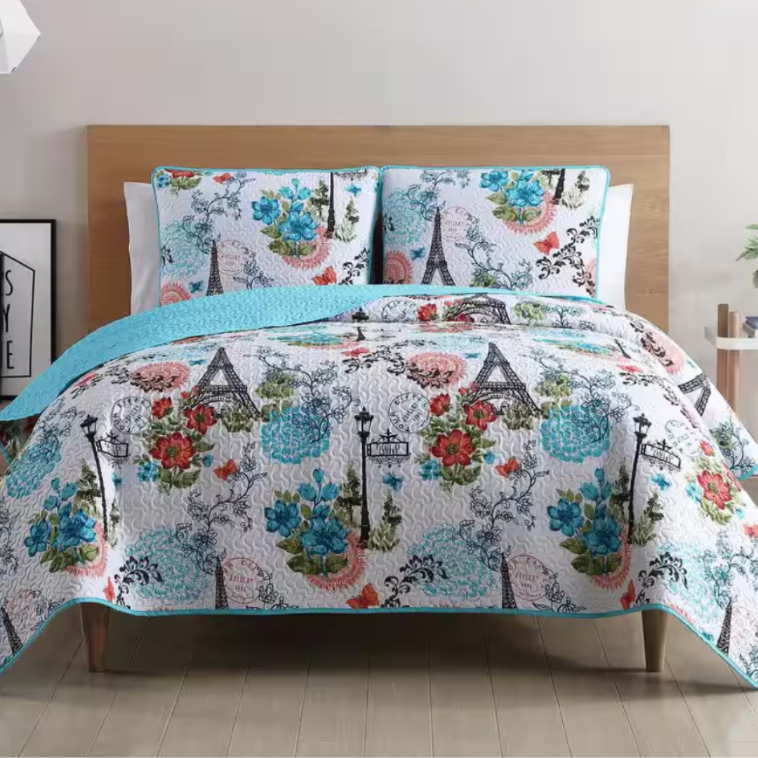 A quilt and pillow set featuring Parisian-themed designs with the Eiffel Tower, flowers, and vintage streetlights, accented with blue, red, and green colors.
