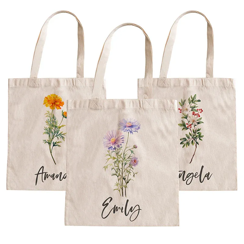 Three beige tote bags with floral designs and personalized names: Amanda, Emily, and Angela. Each bag features a different flower illustration in the center.