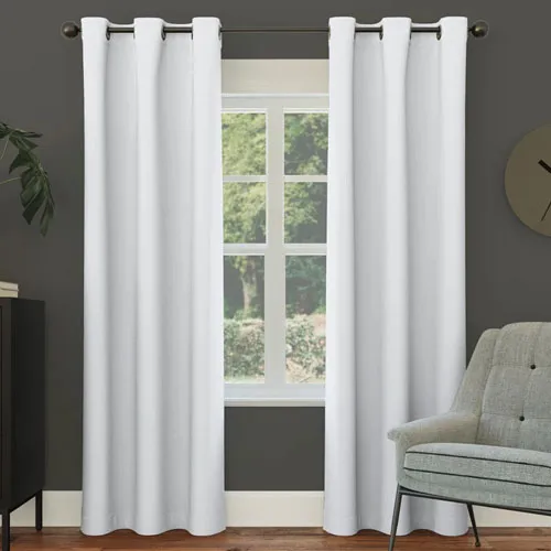 White grommet curtains hanging on a dark rod against a gray wall, with a window view of greenery and part of a gray upholstered chair visible on the right.