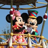 Mickey and Minnie Mouse characters dressed in colorful costumes are standing on a decorative parade float.