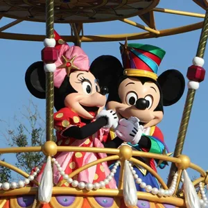 Mickey and Minnie Mouse characters dressed in colorful costumes are standing on a decorative parade float.