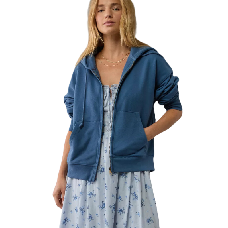 A woman wears a blue zip-up hoodie over a light blue floral dress.