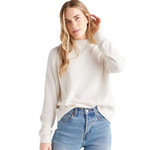 A person is wearing a white, long-sleeve sweater paired with high-waisted blue jeans, standing against a white background.