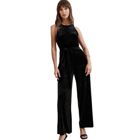 A woman is wearing a sleeveless black velvet jumpsuit with wide-leg pants and a matching tie belt, paired with black high-heeled sandals.