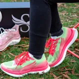 Brightly colored running shoes with red laces are worn on grass, next to a box and a pair of pink sneakers.