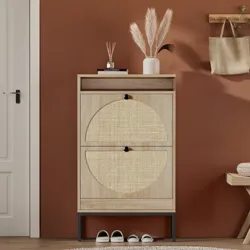 A wooden shoe cabinet with two woven-patterned doors stands against a terracotta wall. It features decor items like a vase with pampas grass on top, shoes underneath, and nearby a bench and a hanging bag.