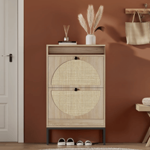 A wooden shoe cabinet with two woven-patterned doors stands against a terracotta wall. It features decor items like a vase with pampas grass on top, shoes underneath, and nearby a bench and a hanging bag.