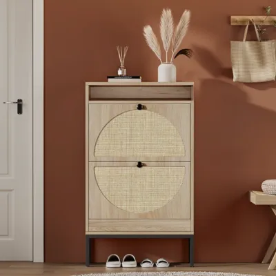 A wooden shoe cabinet with two woven-patterned doors stands against a terracotta wall. It features decor items like a vase with pampas grass on top, shoes underneath, and nearby a bench and a hanging bag.