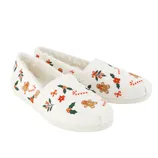 White slip-on shoes with festive embroidery featuring gingerbread men, candy canes, poinsettias, holly leaves, and red bows. They have a plush lining for added comfort.