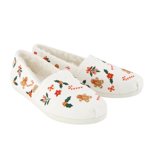 White slip-on shoes with festive embroidery featuring gingerbread men, candy canes, poinsettias, holly leaves, and red bows. They have a plush lining for added comfort.