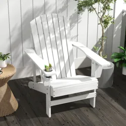 White Adirondack chair with built-in cup holder, placed on a wooden deck next to a rattan side table topped with a plant and book; surrounded by additional potted greenery.