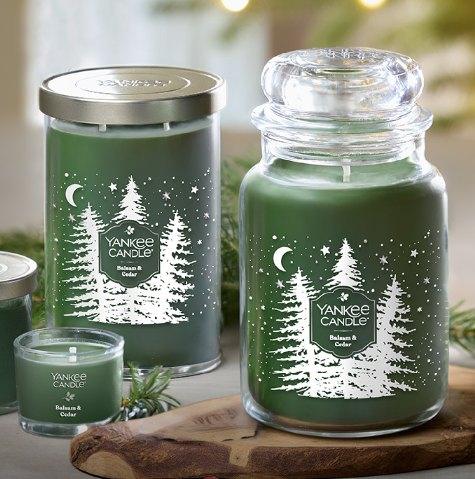Green candles labeled \“Yankee Candle Balsam & Cedar\“ with festive tree and star designs, shown in various sizes including a jar and a votive candle.