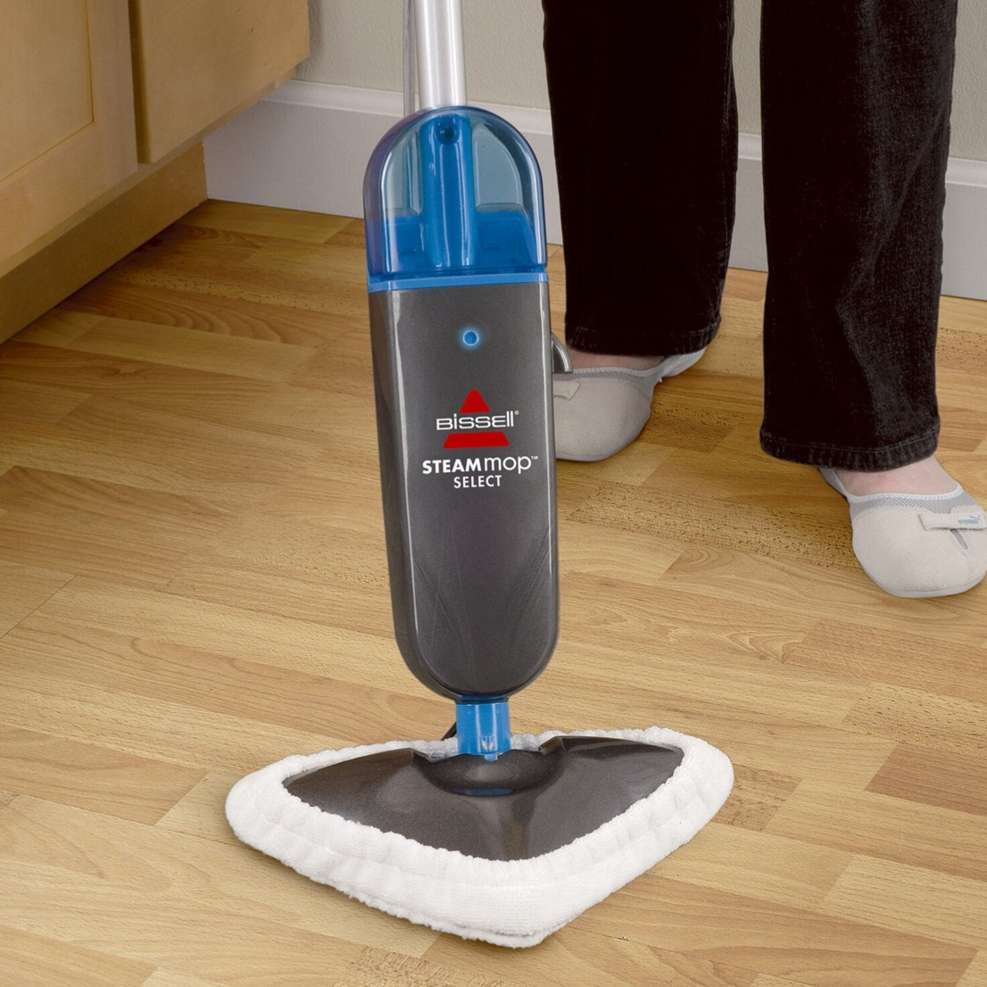 Bissell Steam Mop Select, featuring a triangular mop head with a white cleaning pad, is shown cleaning a hardwood floor.