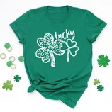 A green t-shirt with two shamrocks, one featuring a leopard print, alongside the word \“lucky.\“ Surrounded by gold coins and additional shamrock decorations.