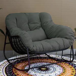 A cushioned dark green rocking chair with a metal frame sits on a patterned round rug with geometric designs in black, white, and orange.