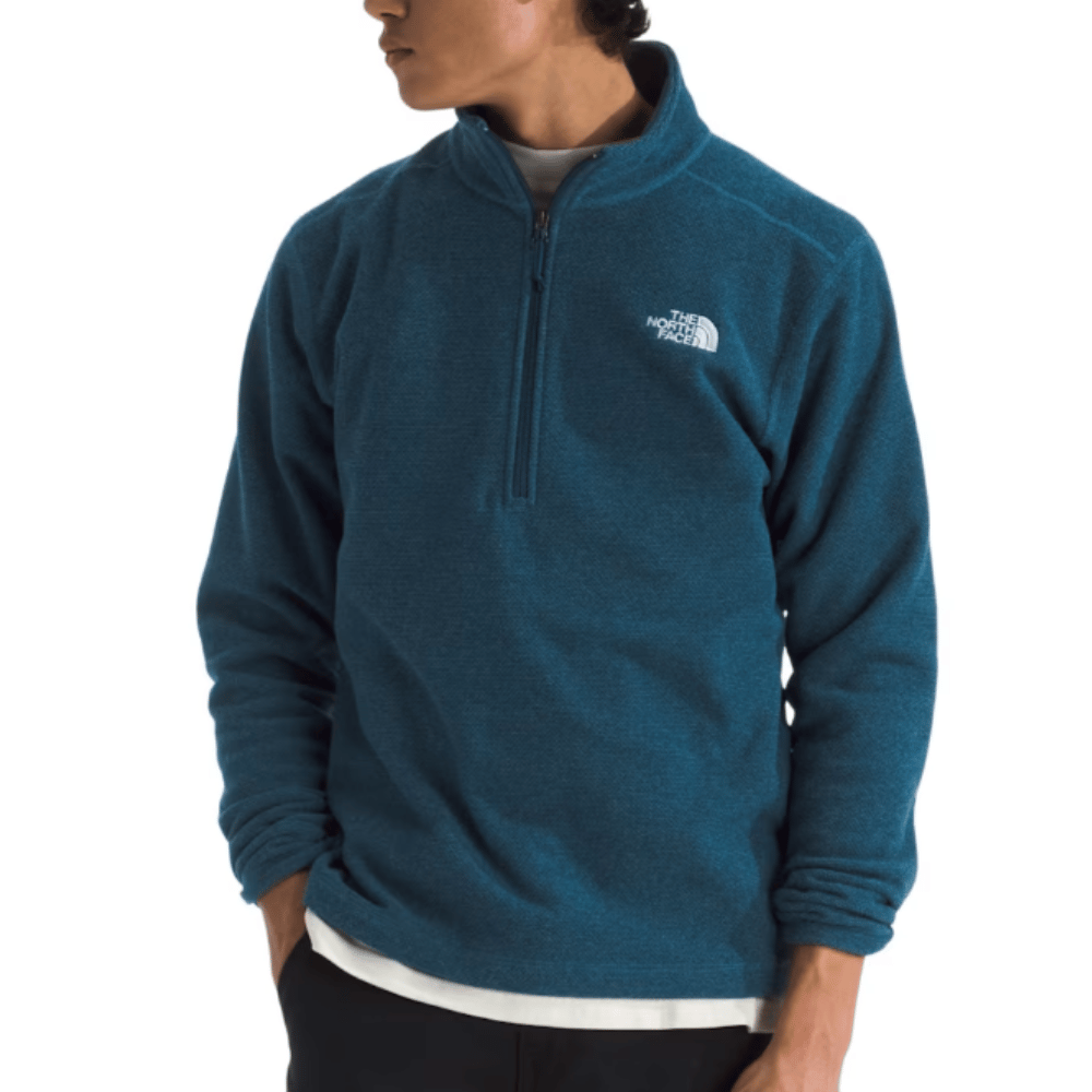 A person is wearing a blue The North Face quarter-zip fleece top with the brand's logo on the left chest. The top is layered over a white shirt and paired with dark pants.