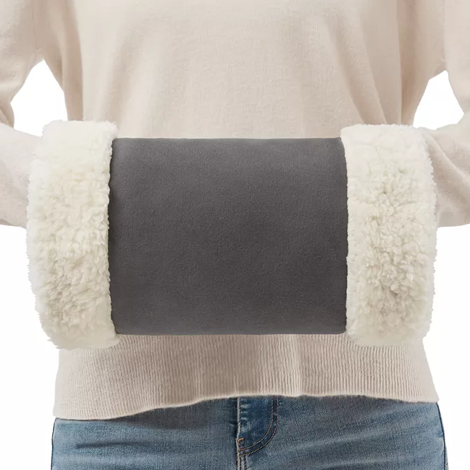 A person is wearing a beige heated hand warmer with fluffy white cuffs on each end, held in front of their midsection.
