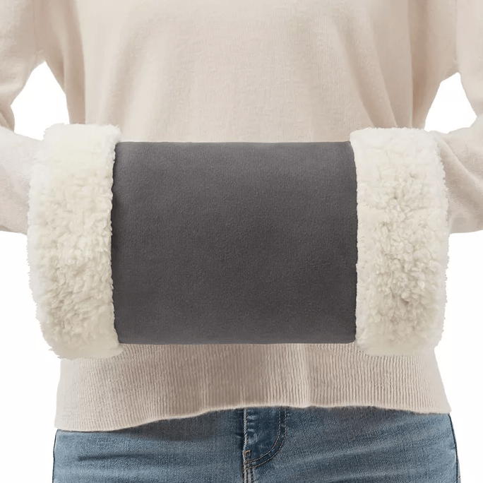 A person is wearing a beige heated hand warmer with fluffy white cuffs on each end, held in front of their midsection.