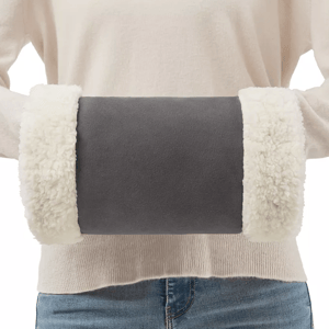 A person is wearing a beige heated hand warmer with fluffy white cuffs on each end, held in front of their midsection.