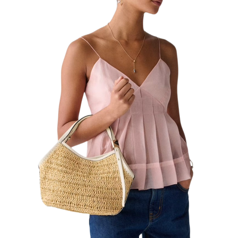 A person wearing a pink spaghetti strap top, blue jeans, and holding a straw handbag with white trim.