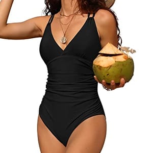 A woman is wearing a black one-piece swimsuit with a V-neckline and ruched waist for tummy control, holding a coconut.