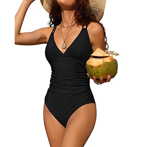 A woman is wearing a black one-piece swimsuit with a V-neckline and ruched waist for tummy control, holding a coconut.