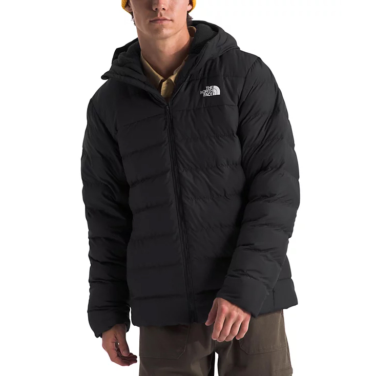 A person wearing a black, hooded North Face puffer jacket, paired with khaki pants and a yellow beanie.