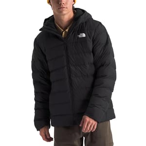 A person wearing a black, hooded North Face puffer jacket, paired with khaki pants and a yellow beanie.