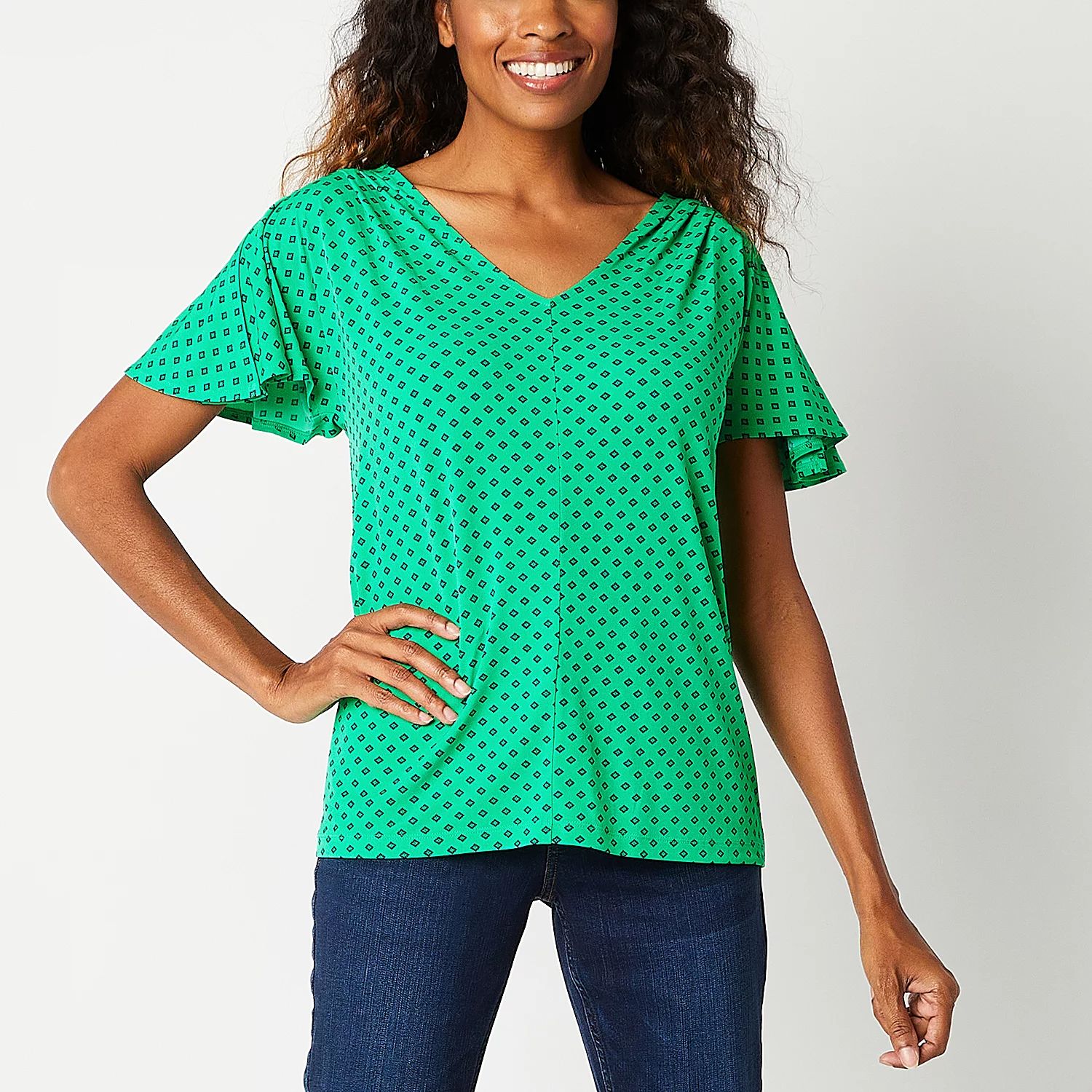 A woman wearing a green, short-sleeved top with a V-neckline and black pattern, paired with blue jeans.