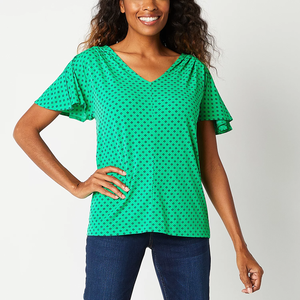 A woman wearing a green, short-sleeved top with a V-neckline and black pattern, paired with blue jeans.
