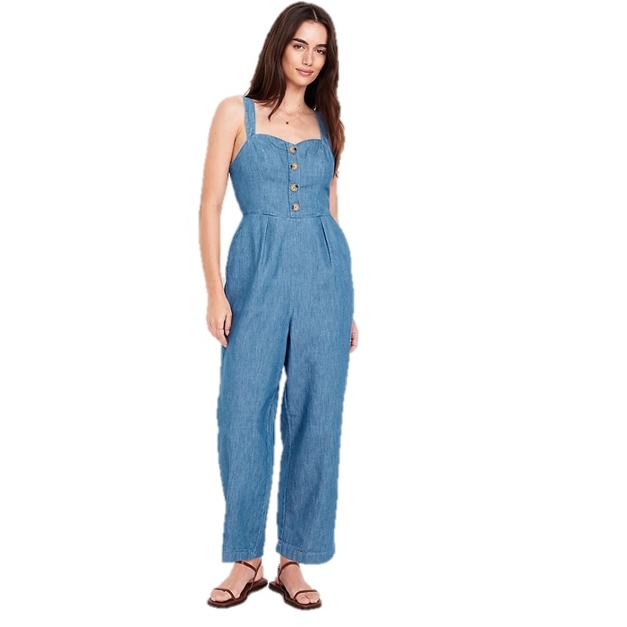 Sleeveless denim jumpsuit with button detailing and wide-leg fit, paired with simple sandals.