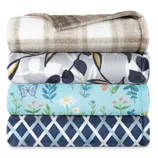 Four folded blankets in different patterns: a plaid design, a floral pattern with yellow and blue leaves, a light blue blanket with butterflies and flowers, and a navy geometric print.