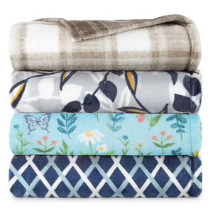Four folded blankets in different patterns: a plaid design, a floral pattern with yellow and blue leaves, a light blue blanket with butterflies and flowers, and a navy geometric print.